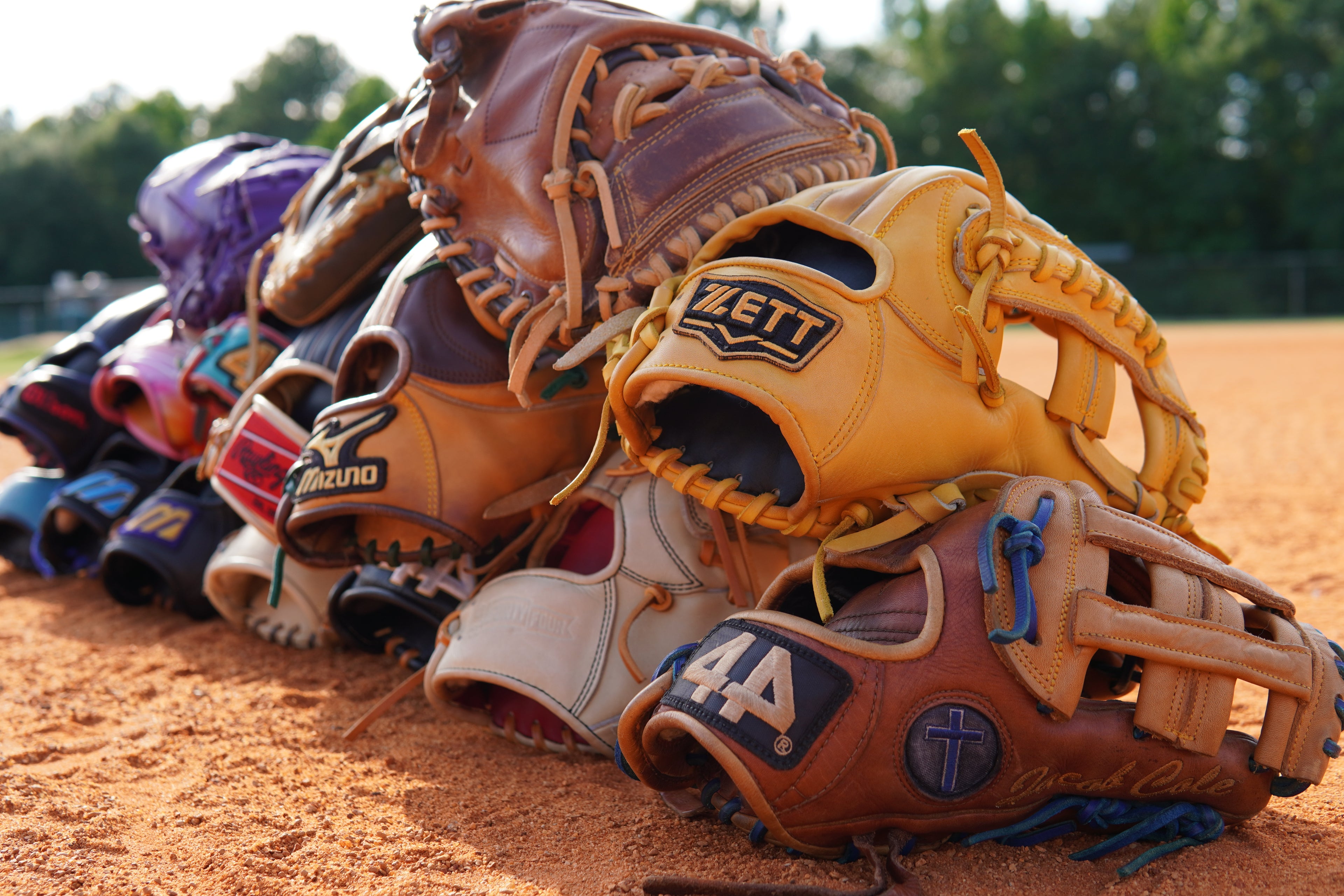 Collection of baseball gloves with visible brand logos on a dirt surface.